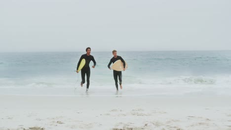 front view of two male surfer running together with surfboard on the beach 4k