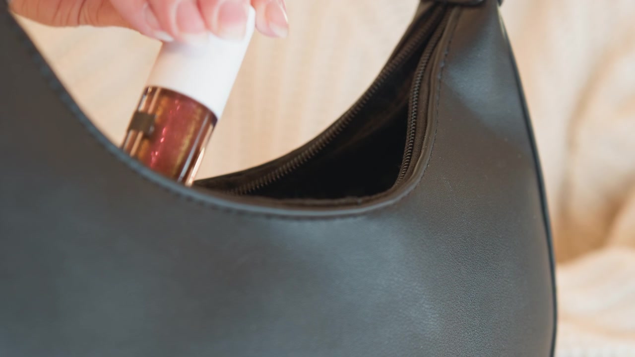 Primo piano di una mano che inserisce una piccola bottiglia nell'apertura di una borsa in pelle testurizzata, con una presa attenta delle dita, cucitura visibile, luce soffusa, fodera interna e un movimento sottile che suggerisce un imballaggio di routine o.