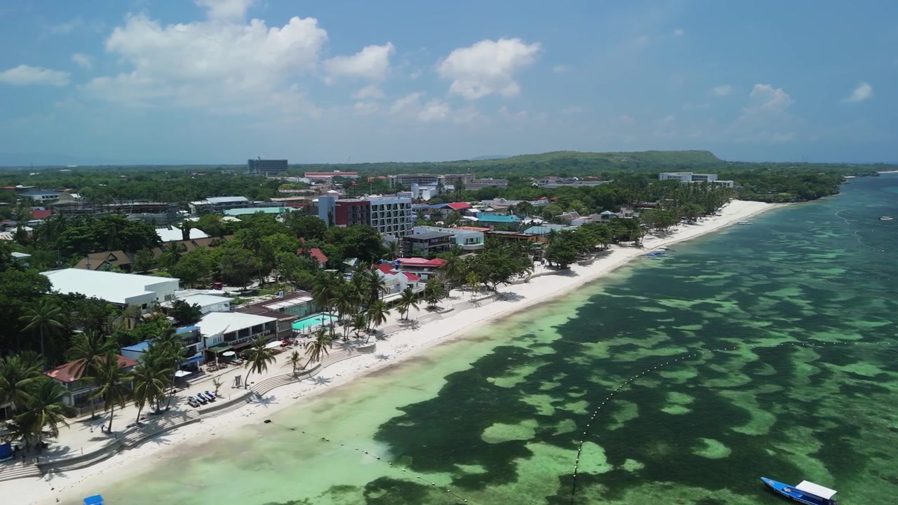 Un drone sorvola e orbita proprio sopra Alona Beach, rivelando sabbia bianca, acqua turchese poco profonda, barche e la costa di Panglao.