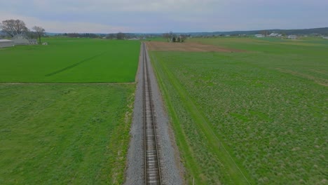 A-Drone-View-Traveling-Along-a-Single-Empty-Rail-Road-Track-That-Goes-Thru-Green-Farmlands-on-a-Spring-Day
