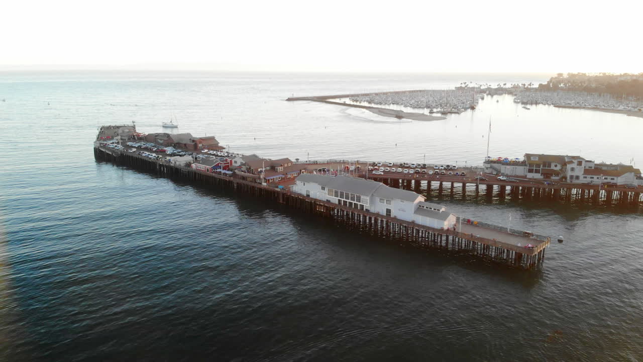 Kaliforniya, Santa Barbara Limanı'na doğru Pasifik Okyanusu'nda seyreden Stearns Wharf iskelesi ve yelkenli teknelerin havadan drone çekimi.