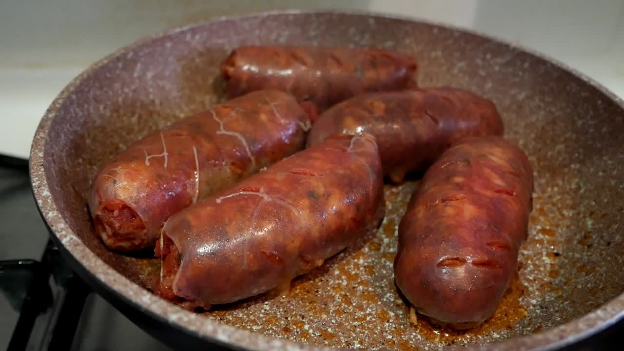 primer plano de algunas salchichas de chorizo rojas grandes y brillantes que se cocinan en una sartén