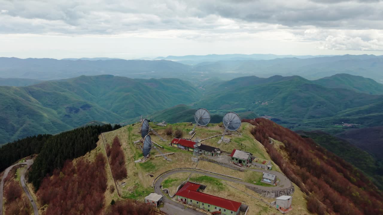 Old radar station on a mountain peak, surrounded by vast green hills, aerial view