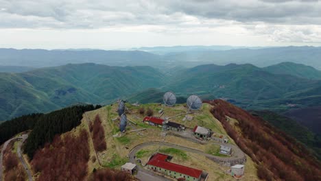 old radar station on a mountain peak, surrounded by vast green hills, aerial view