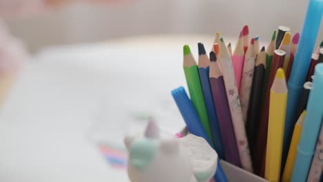 young girl sitting at a table, drawing with colorful crayons. ideal for themes of creativity, childhood development, learning, and art activities in a cozy indoor setting.