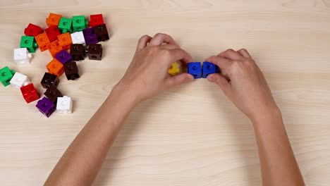 hands assembling colorful cubes on a wooden table