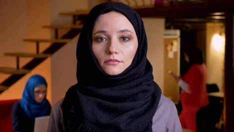 closeup portrait of young beautiful successful muslim businesswoman in black hijab looking at camera being on the workplace indoors