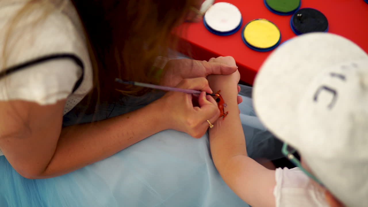 Painting pictures on the skin of a child,  the girl paints with paints on the child's forearm, small boy with cap