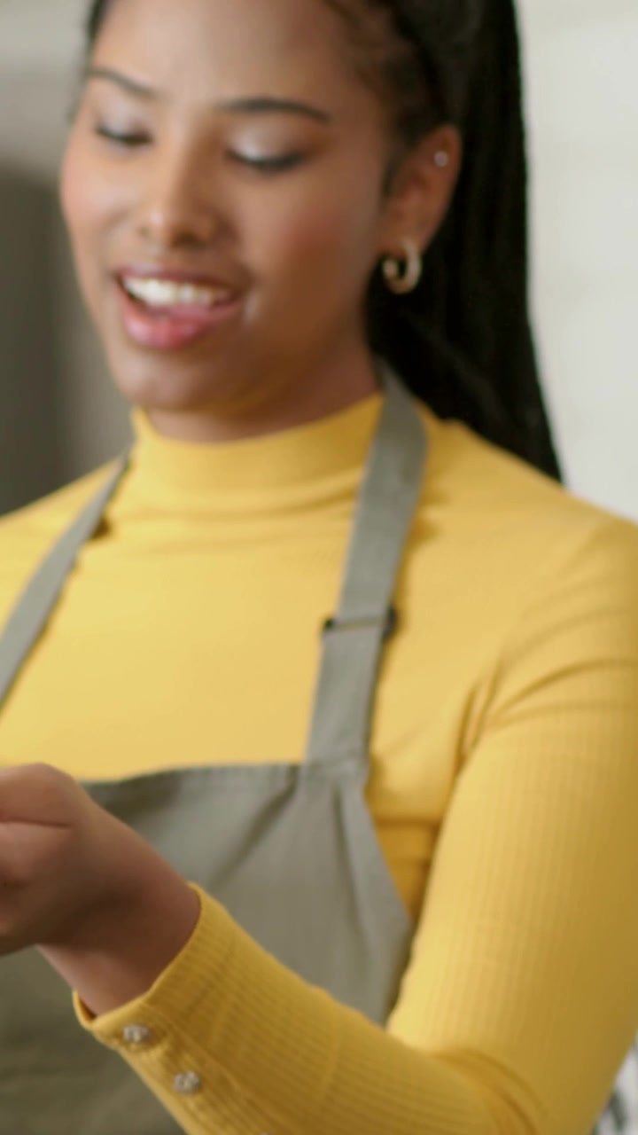 Vertical video: Extending, cook wearing mustard top gray apron examining item for demo at counter