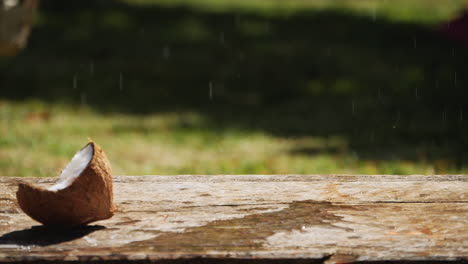 Frische-Kokosnuss-Fällt-Auf-Einen-Holztisch-Und-Teilt-Sich-In-Zwei-Hälften,-Wobei-Kokoswasser-Verschüttet-Wird