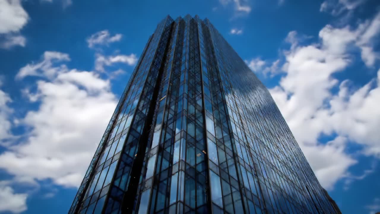 Dramatic Angle of a Tall, Modern Glass Building Reaching Towards a Bright Blue Sky with Fluffy White Clouds; Captures Urban Architecture and Contemporary Design in Vibrant Detail