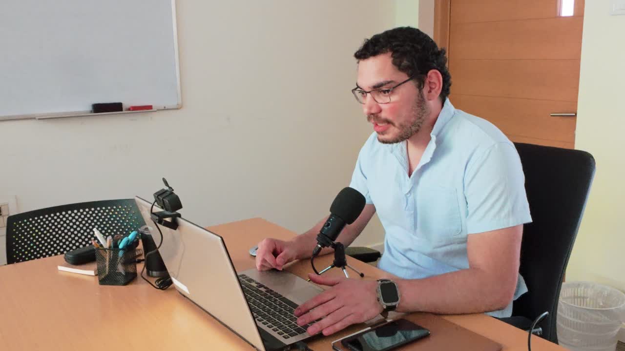 un hombre está sentado en un escritorio con una computadora portátil y un micrófono