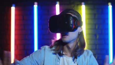 close up view of young man in vr glasses and moving like scared in a room with colorful neon lamps on the wall