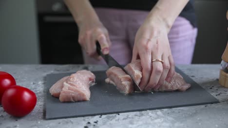 mujer cortando pecho de pollo crudo en una tabla de cortar