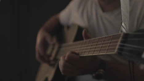 man playing and performing on an acoustic guitar with black background and soft warm light