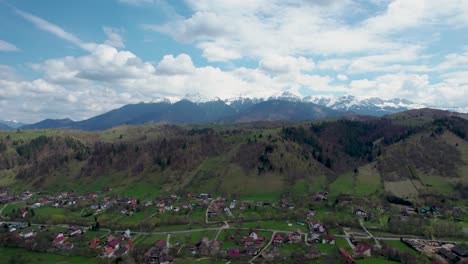 Vista-De-Drones-De-Las-Majestuosas-Montañas-Bucegi,-Con-Parches-De-Nieve,-Pintoresco-Pueblo-De-Montaña-Y-Campos-Verdes,-Rumania,-Transilvania,-Moieciu,-Rucar,-Bran