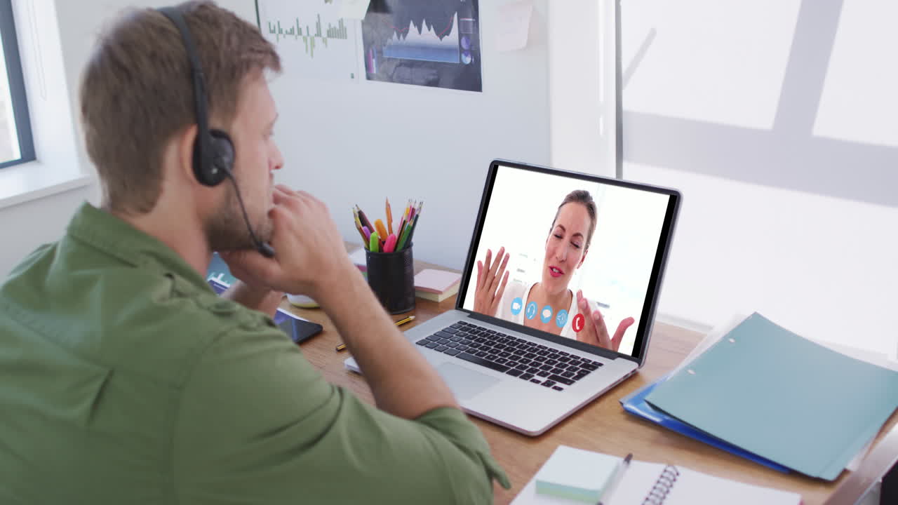 Kaukasisk mand bruger bærbar computer og telefonheadset på videoopkald med en kvindelig kollega.