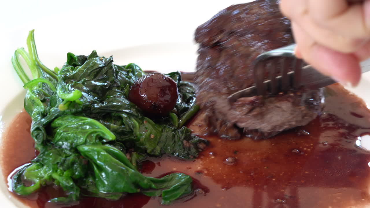 Woman cutting up a cooked beef tenderloin in sauce with greenery on a white plate