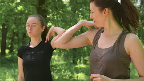 zwei glückliche hübsche läuferinnen wärmen sich auf und strecken ihre schultern im park