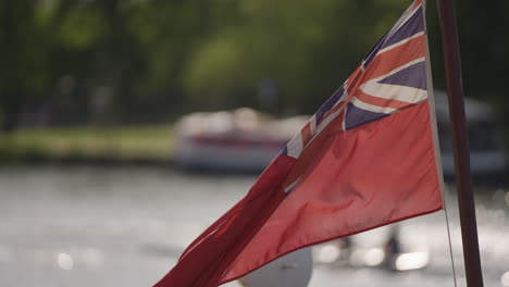 red ensign uk flag waving in light breeze on sunny day with water in background