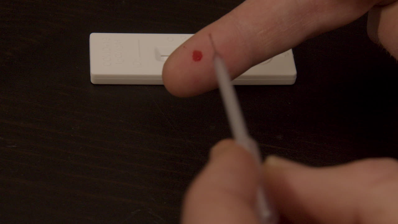 pipette sucking up drop of blood from finger in preparation of Covid-19 self test - close