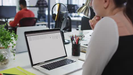 mujer caucásica sentada en un escritorio viendo el procesamiento de datos de codificación en la pantalla de una computadora portátil