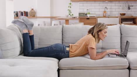 mujer relajada acostada en el sofá en casa trabajando en una computadora portátil
