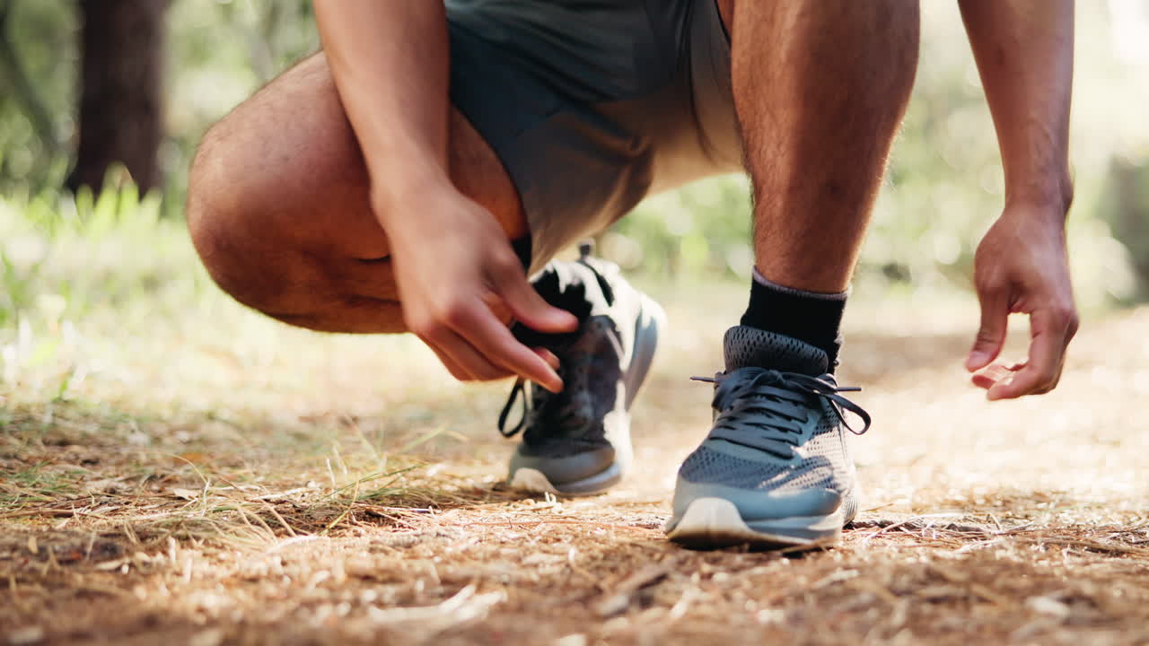 Uomo che si allaccia i lacci delle scarpe da corsa su un sentiero nel bosco all'aperto