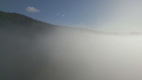 rising drone shot of lake district fells as drone rises through cloud inversion on sunny autumnal morning with blue sky and white clouds