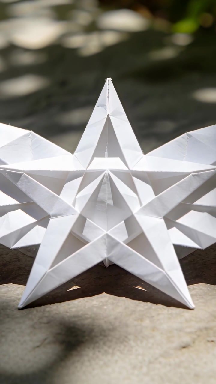 Vertical video: Moving dappled sunlight across white origami star on stone, showing crisp shadows