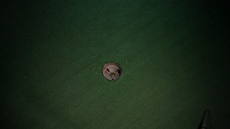 a wide shot of a yellow mini golf ball going in the hole