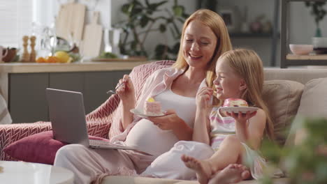 pregnant woman watching moving on laptop with daughter