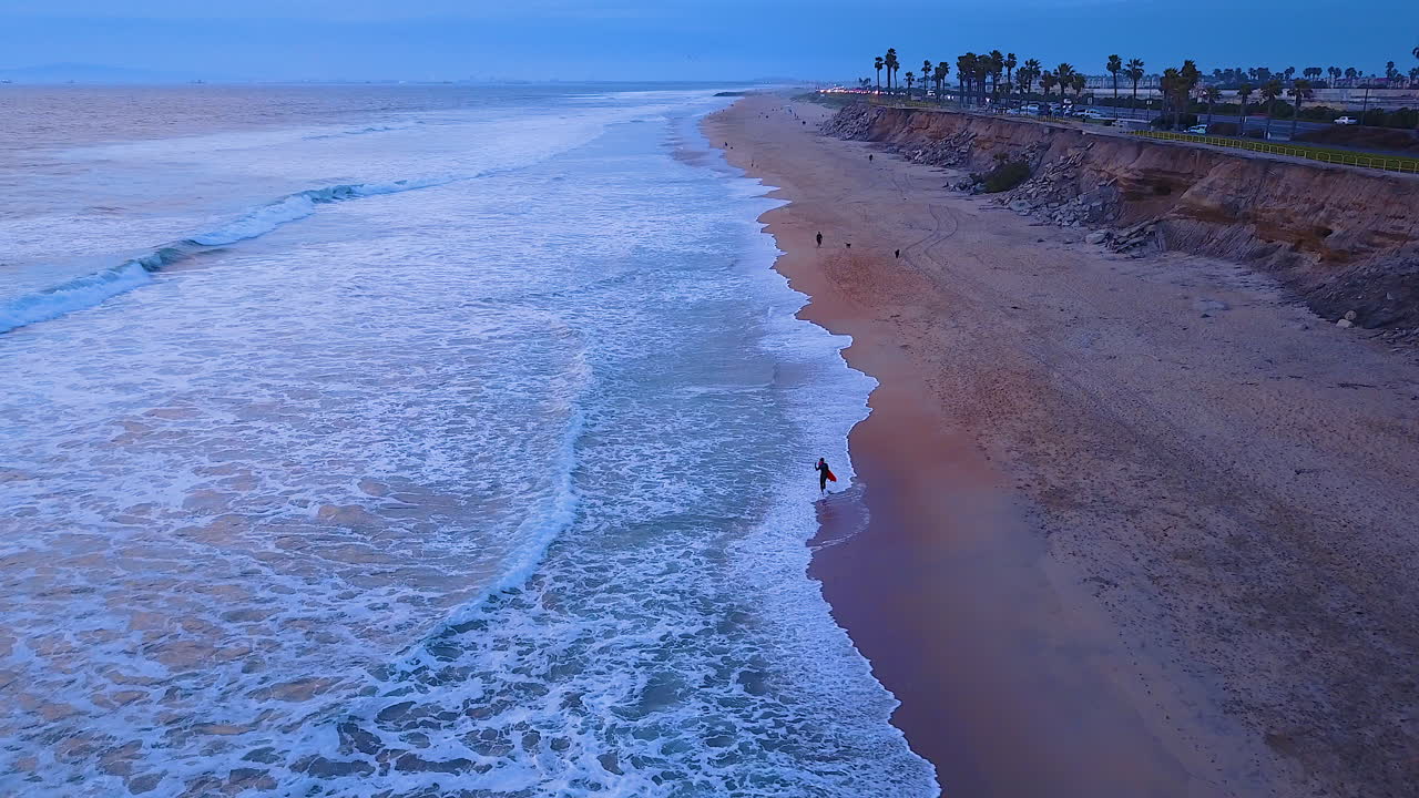 серфингист идет по пустому пляжу перед заходом солнца