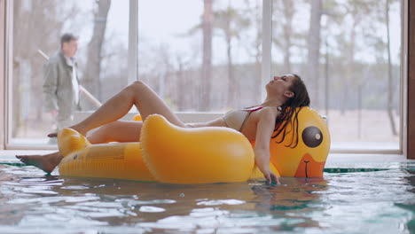 adult woman is relaxing in pool lying on inflatable swimming circle like yellow duck and meditating