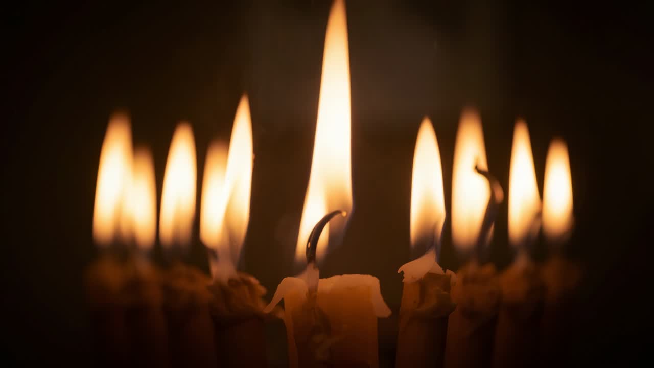 Nove sottili fiamme di candela che danzano sotto le correnti d'aria nello spazio oscuro, stoppini incandescenti che gocciolano cera