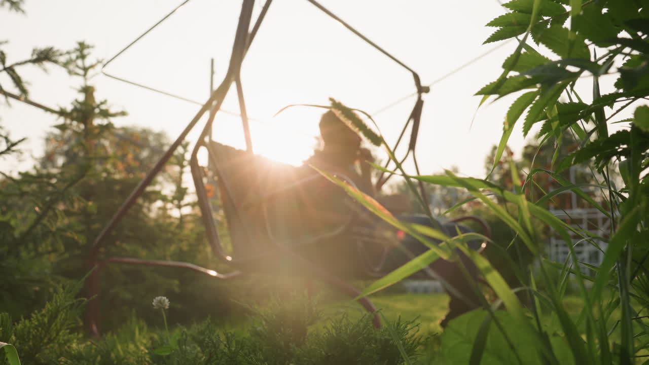 golden sun rays illuminate man seated on swing bench eating freshly harvested strawberries picked from lush garden while serene orchard backdrop glows with warm afternoon light