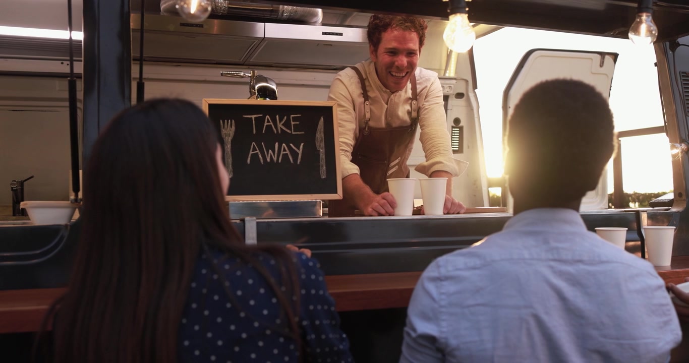Smiling Food Truck Vendor Serving Diverse Customers at Sunset
