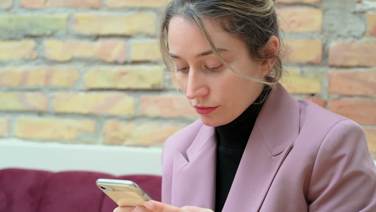 Close up of a woman in a pink blazer typing on her phone in a restaurant