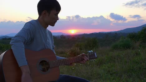 close up of asian man playing guitar at sunset and horizon in background, vietnam