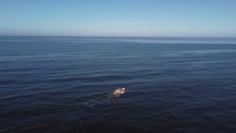 aerial view of a small boat in the middle of a calm and immense sea, sailing towards the horizon