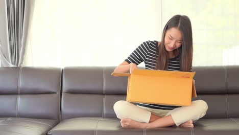 asian young woman happily opens yellow post box and showing happy face expression while sitting on a couch daytime