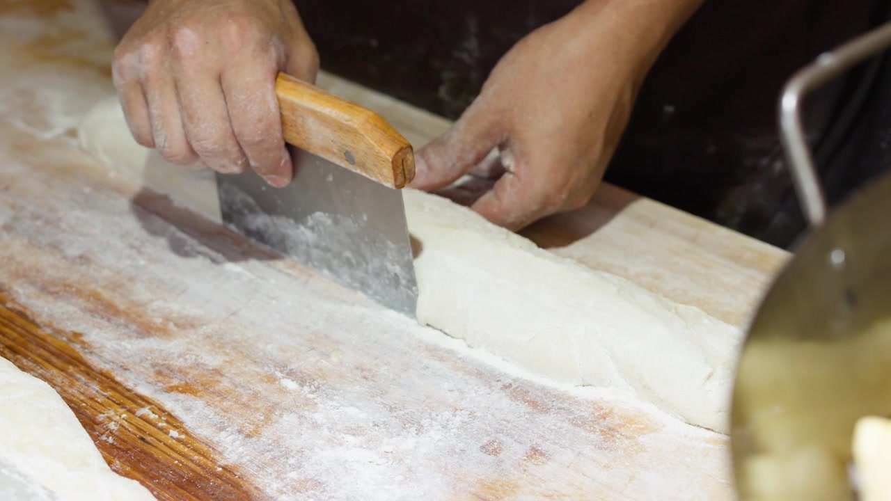 Primo piano delle mani di uno chef che impastano la pasta e usano un pennello su una superficie infarinata.