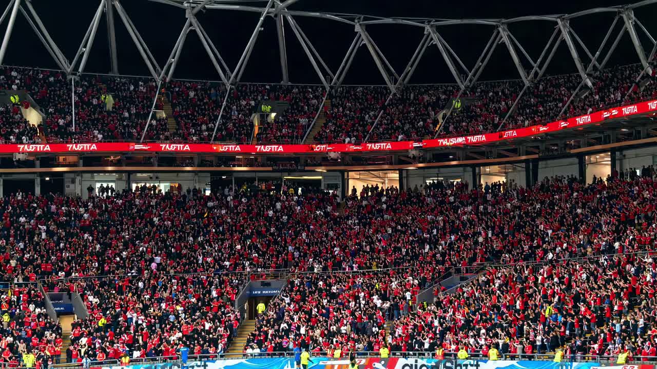 Wide-angle shot of a packed stadium with cheering fans in red, capturing the vibrant atmosphere