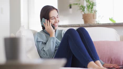 Happy-caucasian-woman-sitting-on-couch-and-talking-on-smartphone