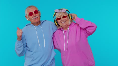 senior modern grandparents pensioners listening music via headphones, dancing disco fooling around