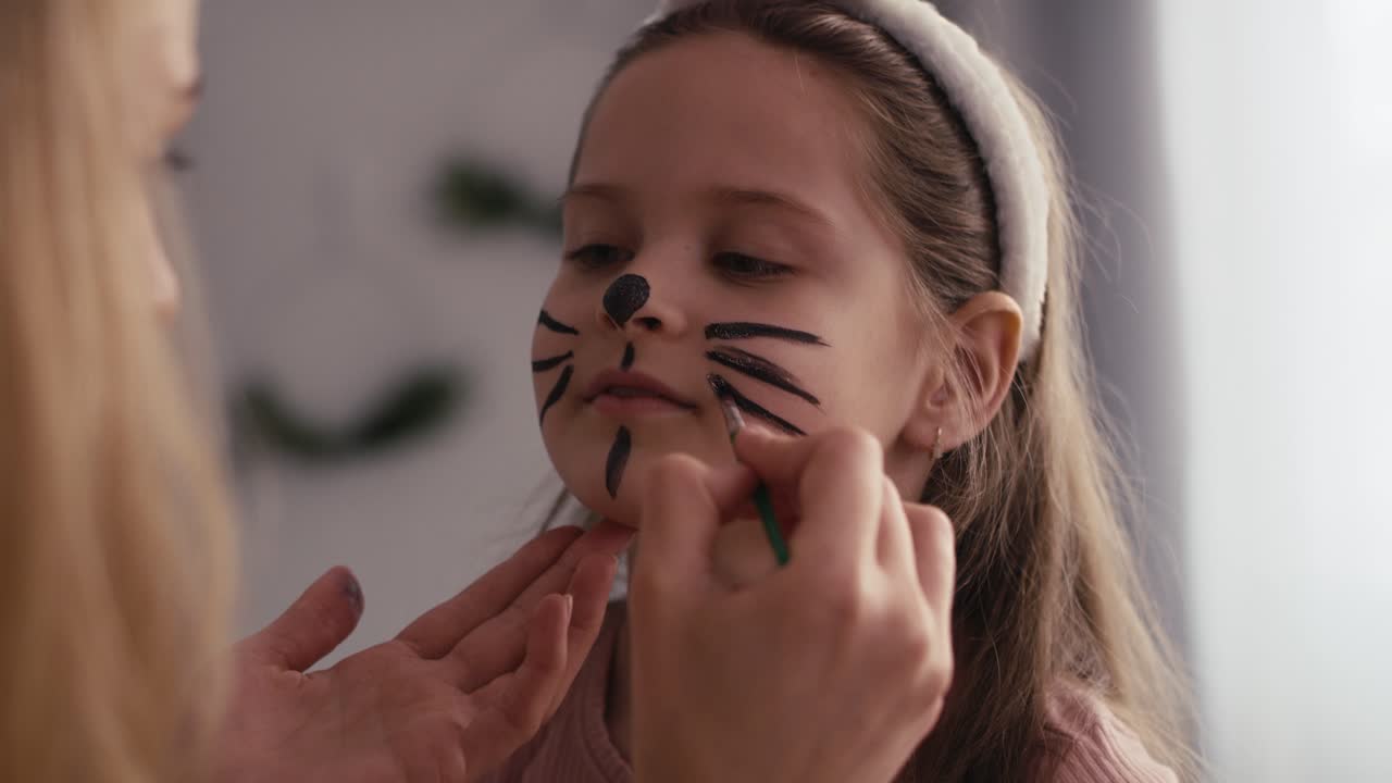 Caucasian mother and daughter painting easter bunny on girl's face.