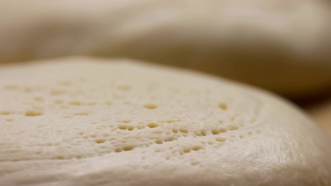 Una prospettiva macro rivela una texture fine e minuscole bolle superficiali su materiale bianco liscio mentre l'illuminazione cambia delicatamente, con messa a fuoco ridotta e toni neutri che enfatizzano motivi visivi dettagliati.