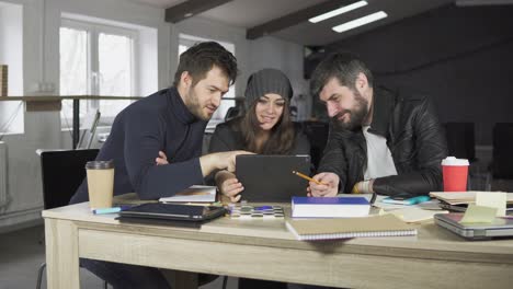 team of young professionals having a meeting in a creative office. looking at the screen of a tablet. business discussion. coffee cups on the table. shot in 4k