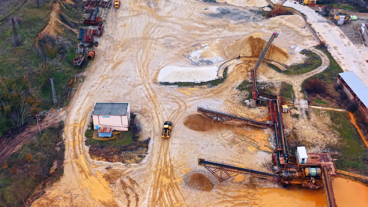 Industrial quarry site with conveyors and machinery. Top down view of an open pit mining operation with yellow machinery, conveyor belts, and piles of sand