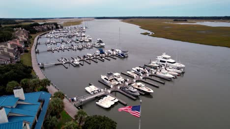 aerial-push-over-flag-flying-in-the-breeze-over-marina-on-bohicket-creek-near-kiawah-island-and-seabrook-island-sc,-south-carolina